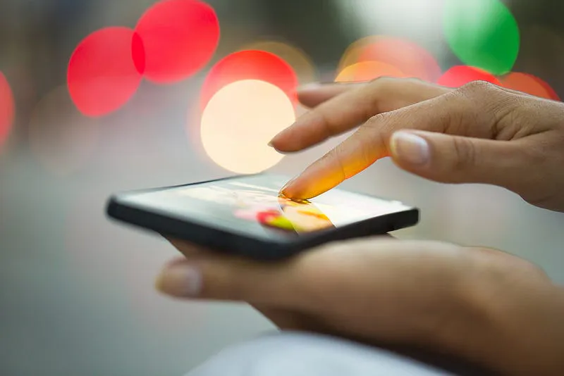 Hand tapping a smartphone touchscreen, illustrating haptic feedback quality in smartphones