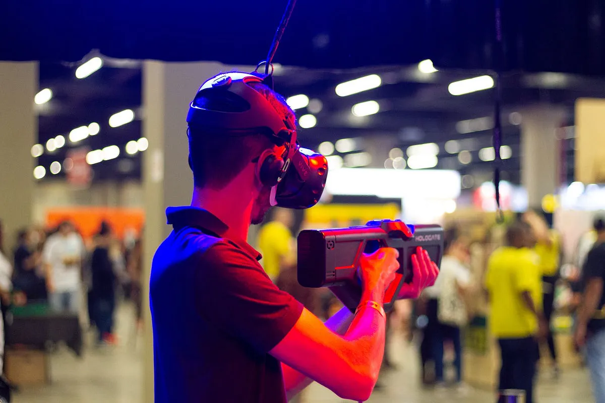 Player in a VR headset aiming a Hologate blaster controller at a gaming event