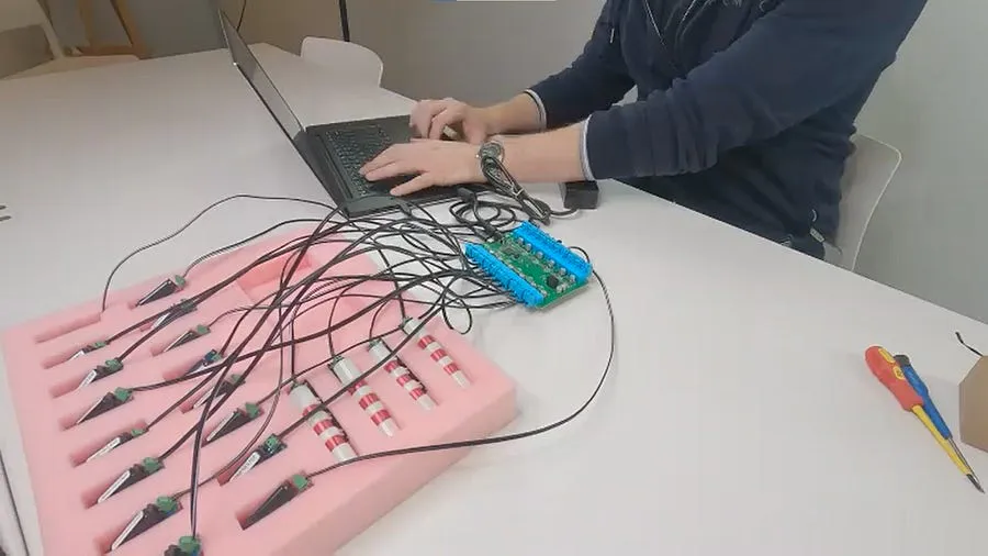 Developer at a laptop driving a multi-channel board wired to a tray of haptic actuators