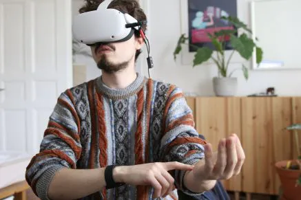 Simon Frübis in a VR headset tapping his wrist, demonstrating his haptic wristband prototype