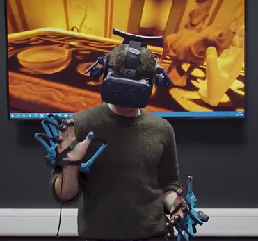 Person in a VR headset and haptic exoskeleton gloves exploring a virtual museum scene with heritage objects