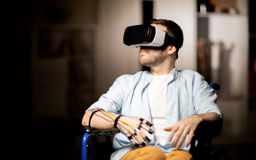 Man in a wheelchair wearing a VR headset and a wired haptic glove for assistive therapy