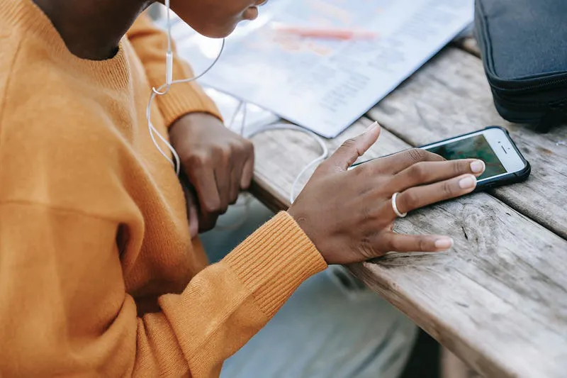 Person with earphones touching a smartphone on a wooden table, illustrating mobile game compatibility